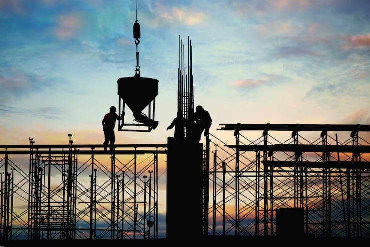 Workers placing concrete from a crane bucket at sunset